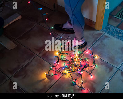 Stringa aggrovigliati di luci di Natale in fondo a una donna e in piedi mentre la decorazione di un albero di Natale Foto Stock