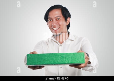 Foto immagine ritratto di un divertente giovani asiatici uomo sorridente felicemente con grandi occhi aperti mentre dando verde regalo scatola di imballaggio Foto Stock