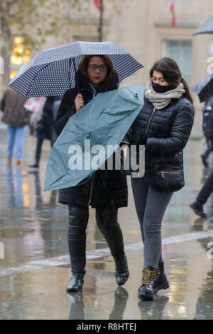 Turisti e londinesi sono visti a Trafalgar Square ombrelli azienda durante un umido, freddo e un giorno blustery a Londra come la neve è scesa in alcune parti della Gran Bretagna. Foto Stock