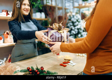 Femmina venditore dà al cliente un regalo di Natale scatola con avvolgimento a mano. Acquirente ordinato un pacchetto di presente, decorazioni di festa Foto Stock