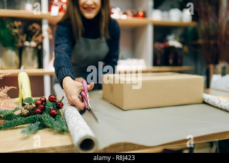 Persona di sesso femminile taglia la carta di avvolgimento con le forbici,  confezione regalo decorazione. La donna avvolge presente sul tavolo,  decorazioni artigianali procedura Foto stock - Alamy