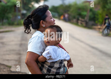 Thakhek, Laos - Aprile 20, 2018: Madre tenendo un bambino al tramonto su una strada in un villaggio del sud Laos Foto Stock