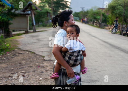 Thakhek, Laos - Aprile 20, 2018: Madre tenendo un bambino al tramonto su una strada in un villaggio del sud Laos Foto Stock