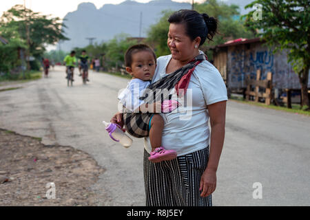 Thakhek, Laos - Aprile 20, 2018: Madre tenendo un bambino al tramonto su una strada in un villaggio del sud Laos Foto Stock