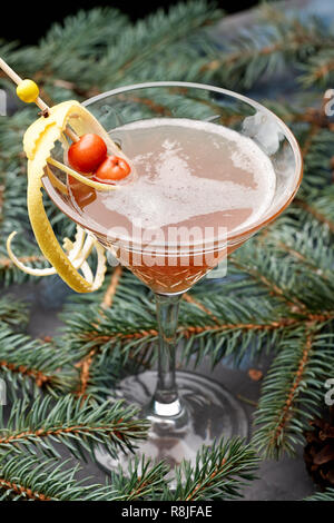 Inverno caldo cocktail Martini in vetro sul ramo di abete. Alcole di vino da bere di Natale con la buccia di limone e frutti di bosco. Lato caldo vista verticale Foto Stock