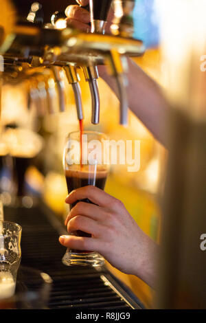 Il barista versa la birra scura da un rubinetto di birra in un bicchiere di birra Foto Stock