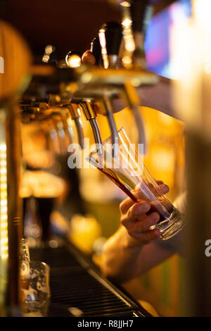 Il barista versa la birra scura da un rubinetto di birra in un bicchiere di birra Foto Stock