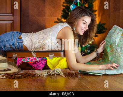 Giovane donna caucasica, turistico nel nuovo anno vicino albero di Natale. allegro e felice, bella ragazza sorriso. Preparazione al Viaggio viaggio. concetto tasse valigia, bagagli. Tenere premuto mappa e rendere piano vacanza festosa. Foto Stock