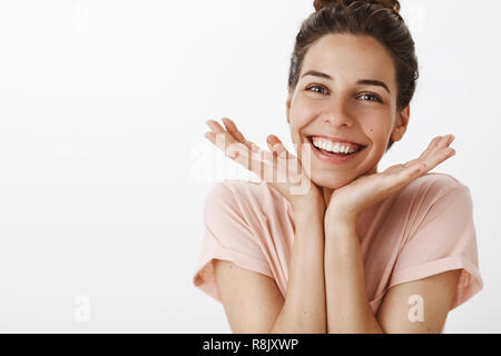 Abbastanza fiducioso e dolce giovane donna elegante con bun gesto avendo cura di pelle la sensazione di felice di liberarsi di imperfactions testa pendente su palme e sorridente ampiamente come gioia dal buon risultato Foto Stock