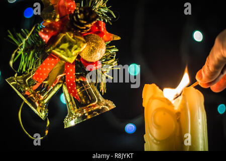 Una scintillante luci di candela una mano con un match. Vicino a dei rami di albero di Natale campane. Foto Stock