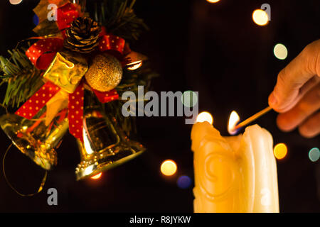 Una scintillante luci di candela una mano con un match. Vicino a dei rami di albero di Natale campane. Foto Stock