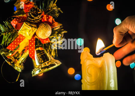 Una scintillante luci di candela una mano con un match. Vicino a dei rami di albero di Natale campane. Foto Stock