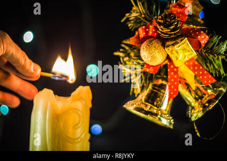 Una scintillante luci di candela una mano con un match. Vicino a dei rami di albero di Natale campane. Foto Stock