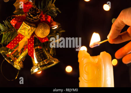 Una scintillante luci di candela una mano con un match. Vicino a dei rami di albero di Natale campane. Foto Stock