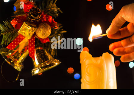 Una scintillante luci di candela una mano con un match. Vicino a dei rami di albero di Natale campane. Foto Stock