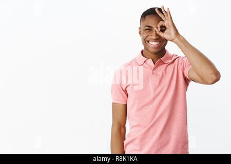 Guy vuoi condividere la felicità con gli altri. Giocoso e divertente bello carismatico americano africano fidanzato sorridente con gioia che esprime un atteggiamento positivo che mostra bene segno over eye e spiata attraverso Foto Stock