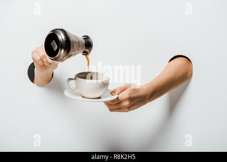 Immagine ritagliata della donna versando il caffè da cezve nella tazza attraverso fori su bianco Foto Stock