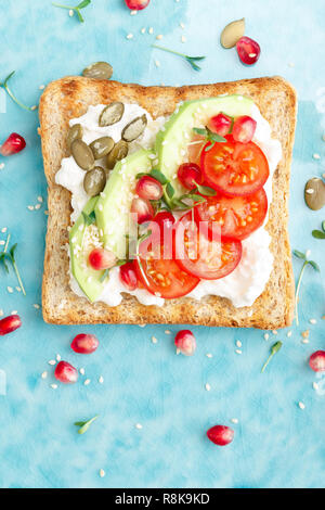 Toast con il formaggio feta, pomodori e avocado, melograno, semi di zucca e i germogli di lino. La dieta la prima colazione. Delizioso e sano cibo. Lay piatto. Parte superiore Foto Stock