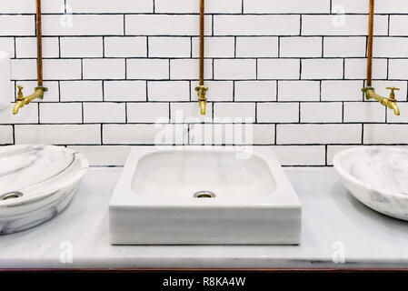 Lavandino di marmo in una toilette pubblica con retro golden rubinetto di acqua con tubi di rame sulla parete con piastrelle bianche, vista frontale con una stanza per il testo Foto Stock