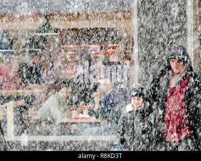 A Belgrado, in Serbia - Dicembre 15, 2018: Padre e figlio egli attraversamento strada di nevicate e di una giovane coppia seduta in un ristorante dietro di loro Foto Stock