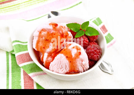 Ice Cream crimson con bacche di lampone, e sciroppo di menta in vaso bianco, un cucchiaio sul tovagliolo sulla luce di legno sullo sfondo della scheda Foto Stock