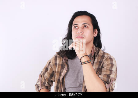 Foto immagine ritratto di un simpatico giovani asiatici studente maschio con capelli lunghi, cercando seriamente, toccando il suo mento e pensare Foto Stock