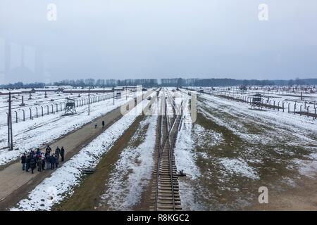 La Polonia, ad Auschwitz e Birkenau, Tedesco campo di lavoro e sterminio nazista (1940-1945), panoramica del camp, i binari della ferrovia, torri di filo spinato e caserma sotto la neve, alcuni visitatori lungo le rotaie di guida Foto Stock