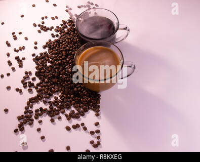 La luce del mattino con angolo di visione di caffè in tazze di vetro con i chicchi di caffè su un tavolo bianco. spazio copia Foto Stock