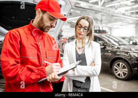 Giovane donna client con la triste emozioni in piedi con meccanico automatico la firma di alcuni documenti presso il servizio auto Foto Stock