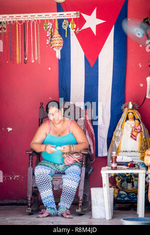 Signora nella parte anteriore della bandiera cubana con icona religiosa in Havana Cuba Foto Stock