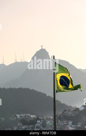 Bandiera brasiliana sventolando come visto dal forte Duque de Caxias in Leme, Rio de Janeiro, Brasile. Favela Babilônia baraccopoli e di Cristo il Reedemer Foto Stock