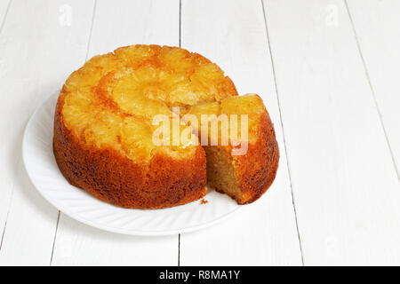 In Casa Ananas Torta rovesciata con un pezzo tagliato su bianco tavolo in legno. Foto Stock