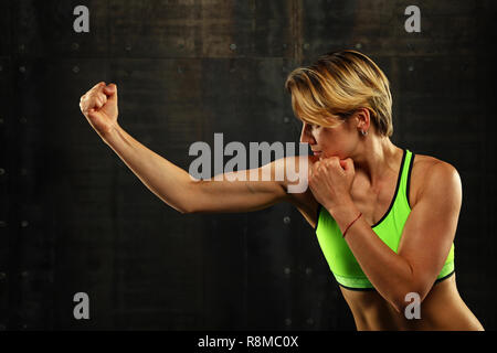 Close up side Visualizza profilo ritratto di una giovane donna atletica shadow boxing in abbigliamento sportivo in palestra su sfondo scuro, guardando lontano Foto Stock
