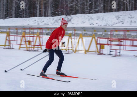 Sciatore luminoso in una giacca rossa e il cappello con un pompon corse su uno sfondo sfocato in motion stadium Foto Stock