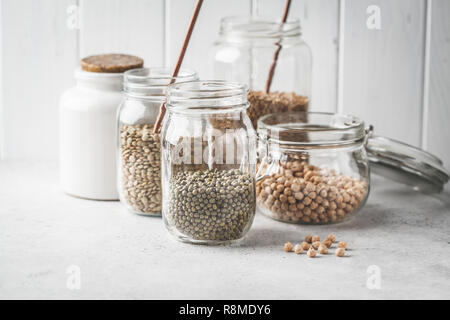 Diversi legumi: fagioli, ceci, grano saraceno, lenticchie in vasetti di vetro su uno sfondo bianco. Una sana alimentazione vegetariana, proteine vegetali, impianto basato die Foto Stock