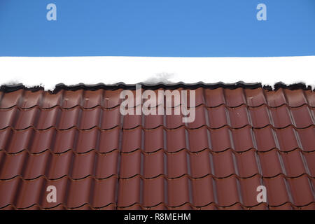 Lato del country house il tetto dalla brown Piastrella in metallo con neve nella soleggiata giornata di primavera sotto il cielo blu con nuvole bianche vista frontale Foto Stock