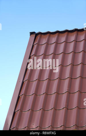 Frammento di country house il tetto dalla brown Piastrella in metallo sotto il chiaro cielo blu senza nuvole. Vista verticale closeup Foto Stock