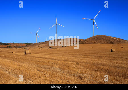 Portogallo Alentejo, Sines. Il potere di vento turbine sollevata al di sopra di un autunno campo agricolo con balle di fieno contro un profondo cielo blu. Foto Stock