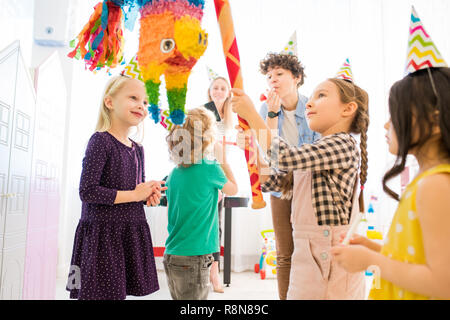 Fiducioso ragazza colpendo pinata colorato a festa per bambini Foto Stock