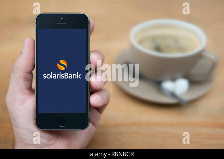 Un uomo guarda al suo iPhone che visualizza la banca Solaris logo (solo uso editoriale). Foto Stock