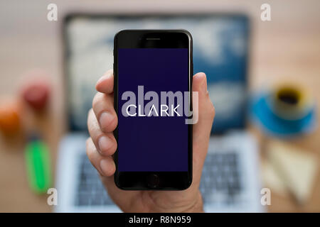 Un uomo guarda al suo iPhone che visualizza il logo di Clark (solo uso editoriale). Foto Stock