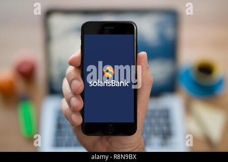 Un uomo guarda al suo iPhone che visualizza la banca Solaris logo (solo uso editoriale). Foto Stock