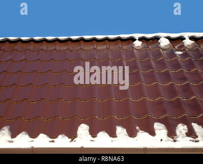 New country house il tetto dalla brown Piastrella in metallo con fusione della neve in primavera sotto il chiaro cielo blu senza nuvole. Vista orizzontale closeup Foto Stock