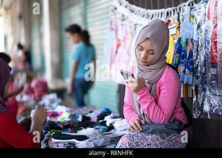 Due filippini ragazze musulmane la vendita di calze su una strada laterale,una delle ragazze utilizzando un telefono cellulare,Cebu City, Filippine Foto Stock