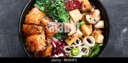 Poke ciotola con il salmone, guinoa, verdure, frutta e tofu su sfondo scuro. Panorama Foto Stock