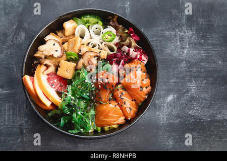 Poke ciotola con il salmone, guinoa, verdure, frutta e tofu su sfondo scuro con spazio di copia Foto Stock