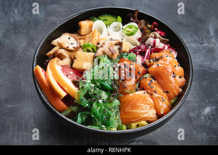 Poke ciotola con il salmone, guinoa, verdure, frutta e tofu su sfondo scuro Foto Stock