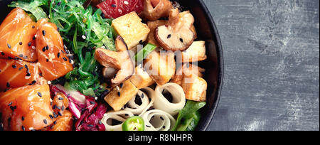 Poke ciotola con il salmone, guinoa, verdure, frutta e tofu su sfondo scuro. Panorama con spazio di copia Foto Stock