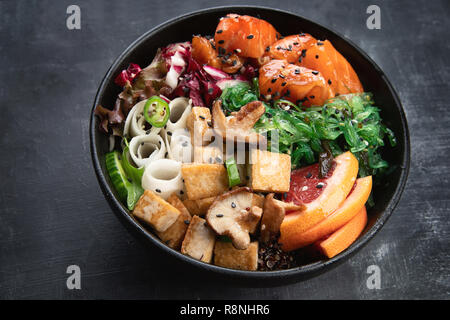 Poke ciotola con il salmone, guinoa, verdure, frutta e tofu su sfondo scuro Foto Stock