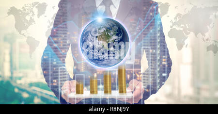 La doppia esposizione di imprenditore della pasticca con la terra e la pila di monete d'oro sul trading grafico sul paesaggio urbano di notte e la mappa del mondo backgr Foto Stock